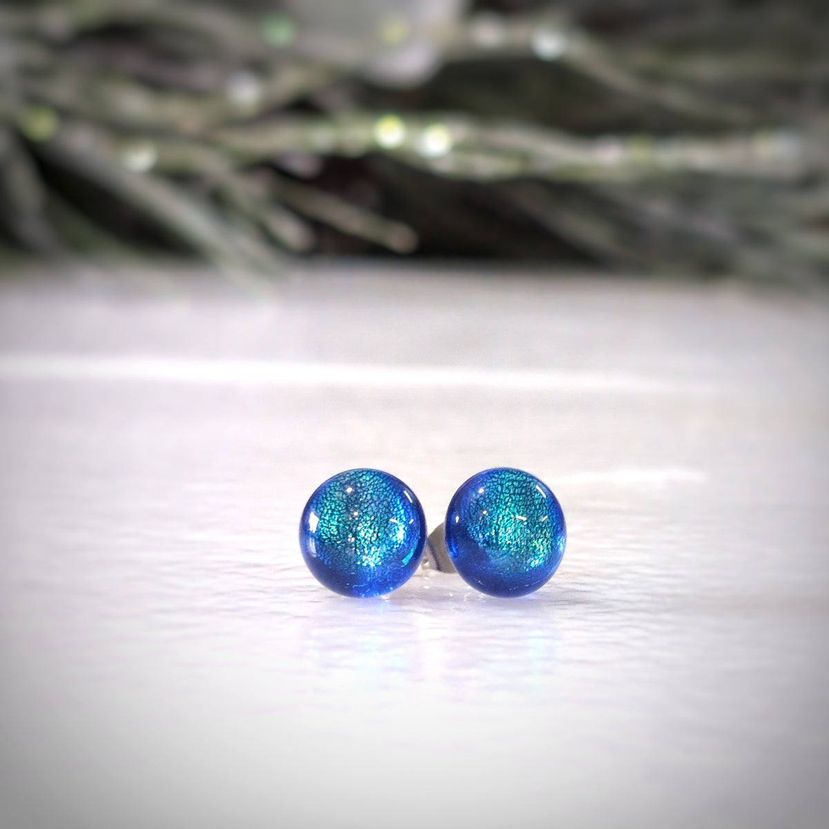 Paire de puces d’oreilles Polaire en verre bleu profond aux reflets turquoise, sur fond blanc.