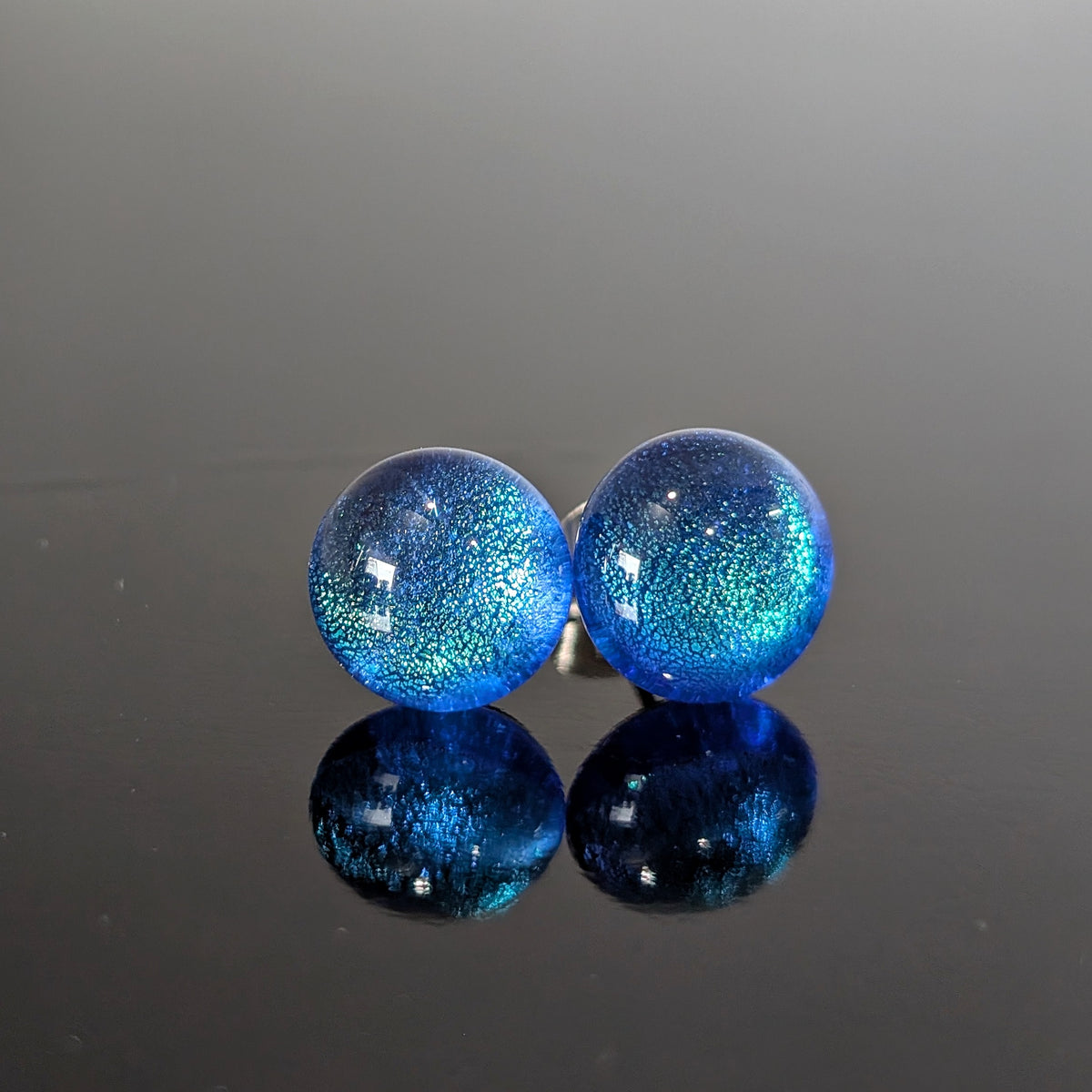 Paire de puces d’oreilles Polaire en verre bleu profond aux reflets turquoise, sur fond blanc.