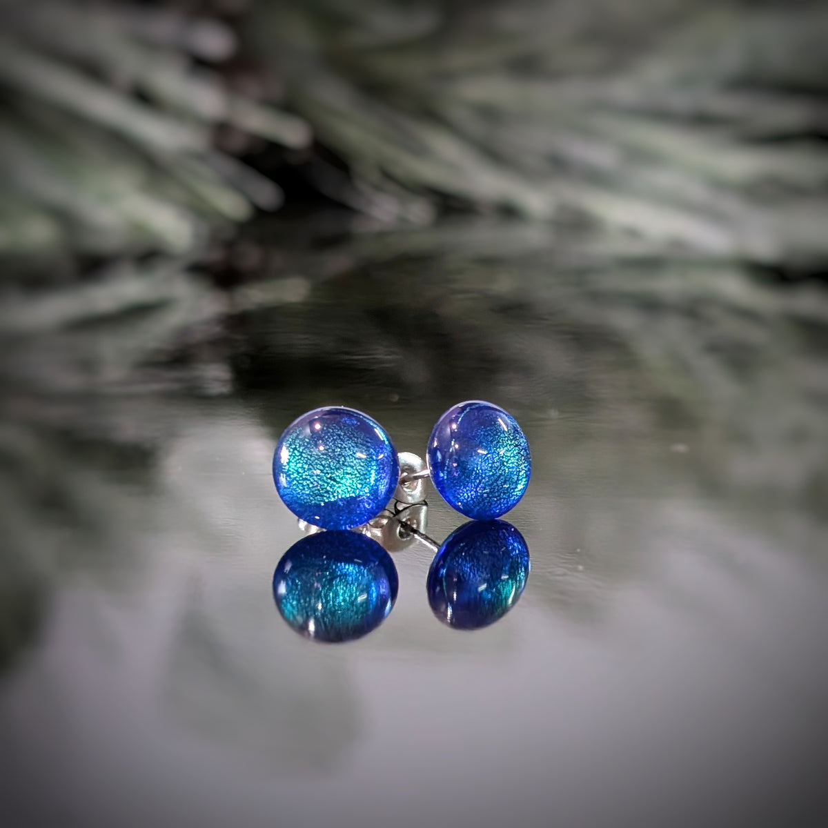 Paire de puces d’oreilles Polaire en verre bleu profond aux reflets turquoise, sur fond blanc.