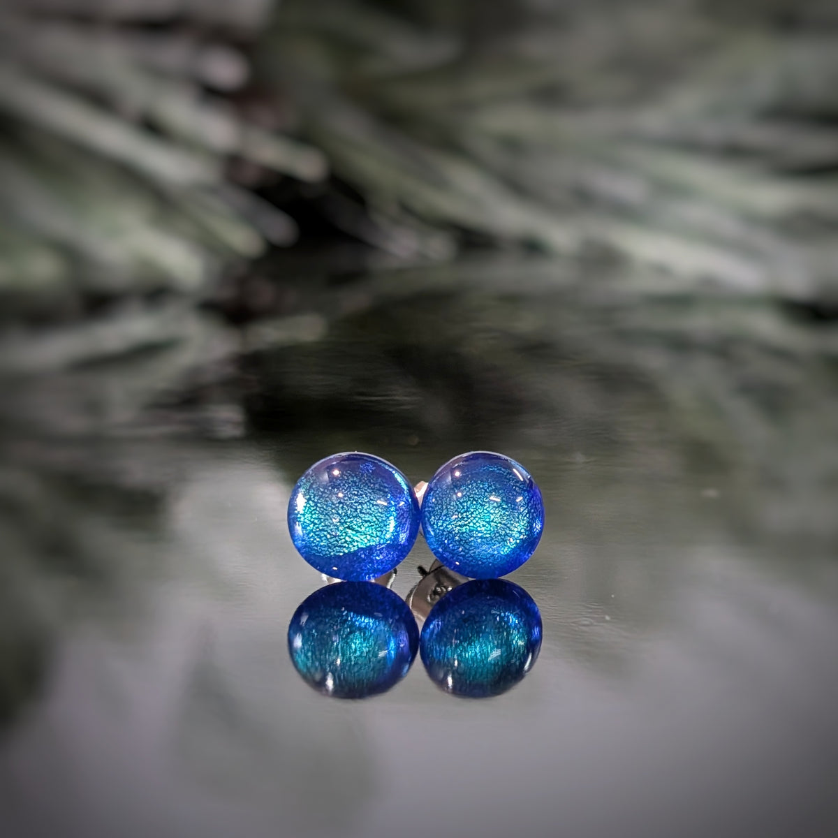Paire de puces d’oreilles Polaire en verre bleu profond aux reflets turquoise, sur fond blanc.